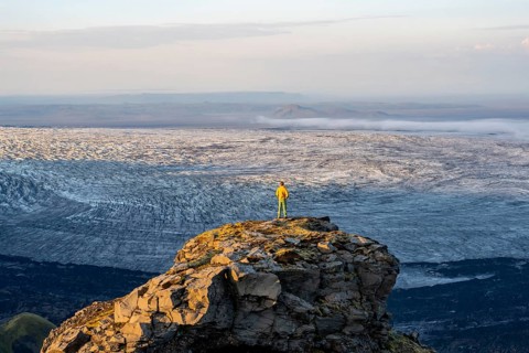 Young man, tourist in front of impressive glacier, in evening light, landscape with mountains and