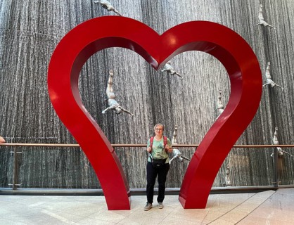 Interior shot, best ager, elderly woman, standing in frame, heart, in front of The Waterfall,