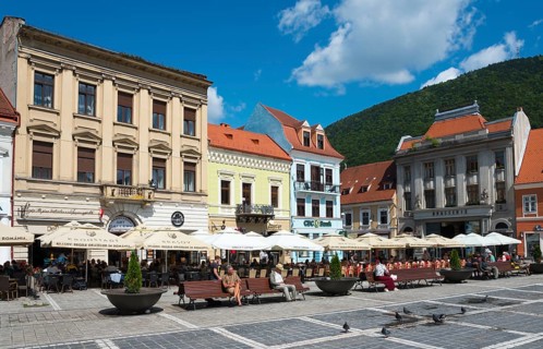 People sitting in outdoor cafés in front of historical buildings on a sunny day in a city, town
