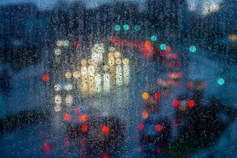 Rainy weather, road traffic, raindrops on a window pane, behind, blurred, lights of vehicles on a
