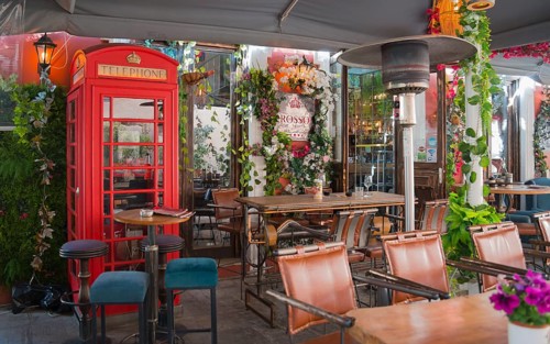 Cosy outdoor café with red British telephone box and lush decoration of plants and flowers,