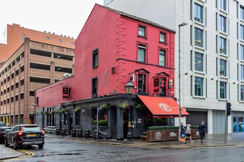 Red building on a street corner with urban flair, cars and a rainy atmosphere, Belfast