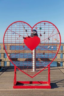 A red heart with padlocks stands on the pier in front of the blue sea horizon, Rügen, Binz