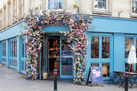 Blue building with colourful flower arch at the entrance of a café, charming city atmosphere, Bath