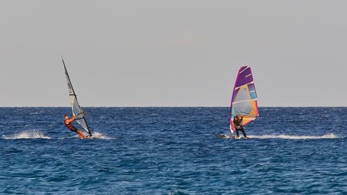 Two windsurfers navigating over the blue sea under clear skies, windsurfing, Meltemi windsurfing