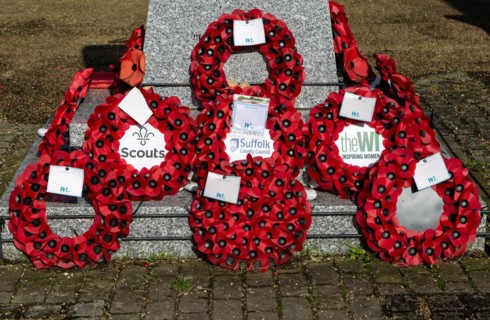 Poppy wreaths at base of war memorial remembrance monument, Saxmundham, Suffolk, England, UK