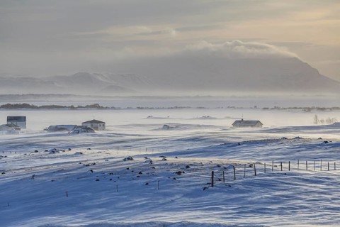 Houses in a snowstorm in front of mountains, windy, sunny, backlight, Myvatn, Iceland, Europe