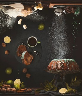 Still life with a cake with chocolate icing surrounded by limes, nuts, cup with coffee, baking