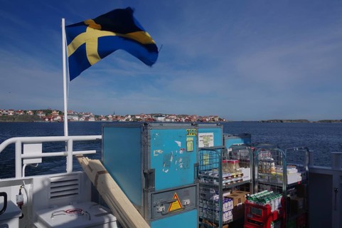Ferry on the sea with Swedish flag, containers and view of a distant city. Clear blue sky and