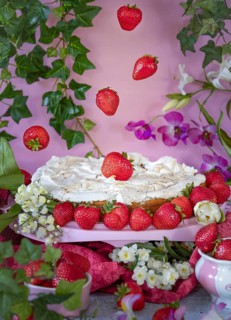 Strawberry cake with meringue decorated with strawberries and flowers against a pink background