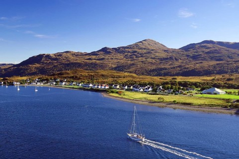 Sailboat on the sea next to a village and rolling hills under a blue sky, autumn, October,