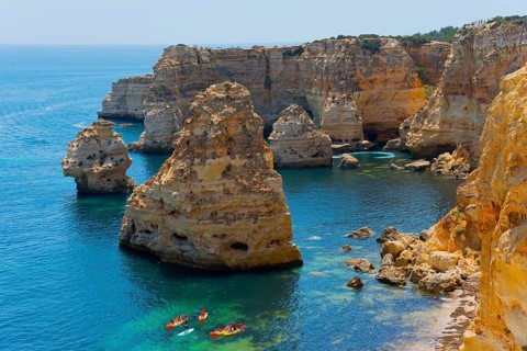 Several kayaks sail along imposing rocks rising from the clear blue sea, Praia da Marinha, Lagoa,