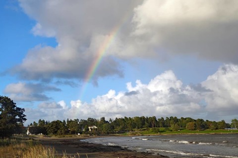 View of the coastal landscape with a rainbow over wooded area under a partly cloudy sky, Tönsberg,