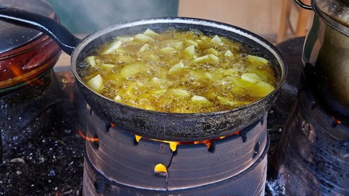 A pan of unpeeled potatoes roasting over an open fire, surrounded by steam, Slowfood Restaurant