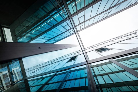 Mirrored glass facades of modern buildings reach up into the sky, reflecting blue and white,