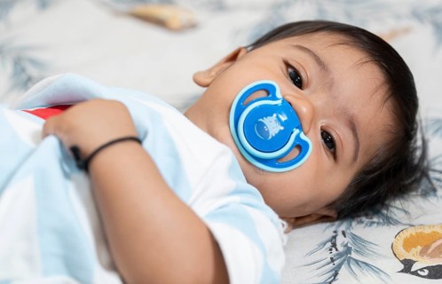 Baby boy playing lying on bed with pacifier on mouth