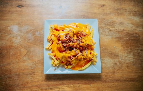 Top view of french fries covered with cheddar cheese and bacon on wooden table. French fries dipped