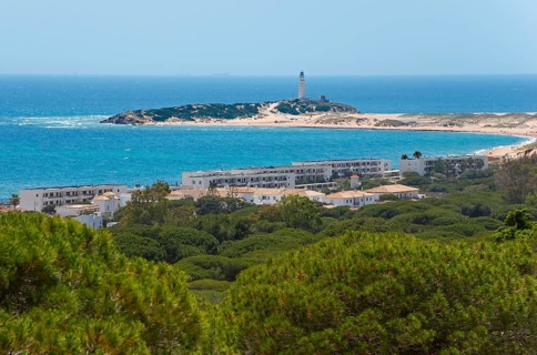Island with lighthouse and white buildings, surrounded by green forest and blue sea, view of Los