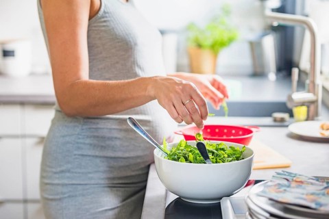 A pregnant woman washes and prepares fresh salad in the kitchen