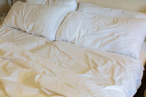 Close-up of rippled and creased white cotton bed sheets and pillows on unmade king size bed, La