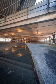 Puddle of water reflects the interior of a multi-storey car park with steel structure, Kaufland