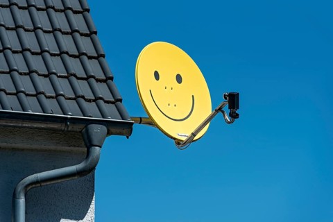 Funny satellite dish, yellow with smiley, satellite antenna on the roof of a house, satellite