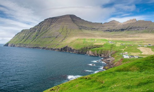 Green coastal landscape with mountains and houses under a blue sky, Vidareidi, Vidoy Island,