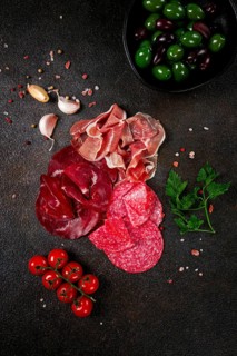Assorted dried meat, fresh tomatoes and olives spread out on a dark surface, food composition, top