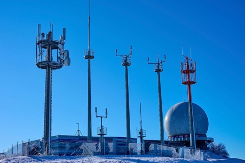 Several transmission masts and a radar station Radom in clear weather with snow and blue sky,
