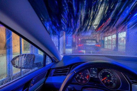 Car in an automatic car wash, car wash tunnel, cleaning foam is sprayed on, rotating brushes clean