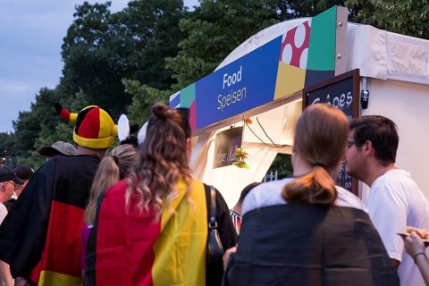 Fans with German flags in front of one of the food stalls in the fan zone at the Brandenburg Tor