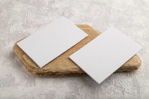 White paper business card, mockup with natural stone on gray concrete background. Blank, side view,