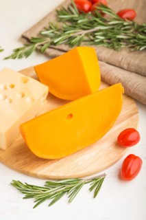 Various types of cheese with rosemary and tomatoes on wooden board on a white wooden background and
