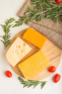 Various types of cheese with rosemary and tomatoes on wooden board on a white wooden background and