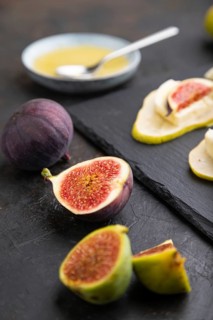 Summer appetizer with pear, cottage cheese, figs and honey on slate board on a black concrete