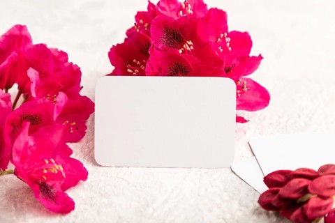 White business card with purple azalea flowers on gray concrete background. side view, copy space,