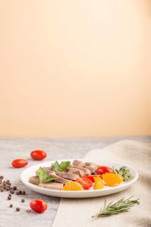 Boiled pork tongue with tomatoes and herbs on a gray and orange background and linen textile. Side