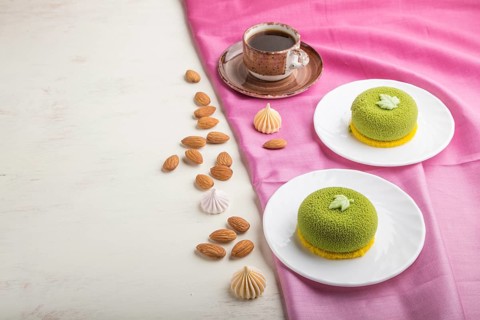 Green mousse cake with pistachio cream and a cup of coffee on a white wooden background and pink
