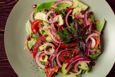 Georgian vegetable salad, tomatoes with cucumbers, red onion, walnut, pomegranate seeds, top view,