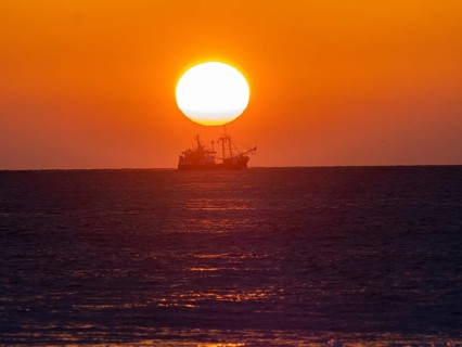 Fishing boat silhouette with a bright sunset backdrop over a calm sea, trawler boat sunset north