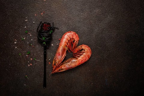 Black spaghetti, wrapped on a fork, langoustines in the shape of a heart, on the table, dish