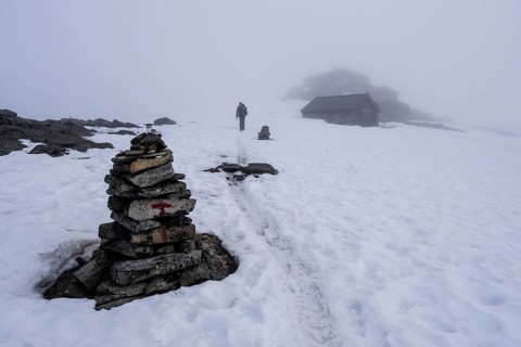 Path on snow between buildings on top of mountain Fannaråken, fog, signpost, single hiker,