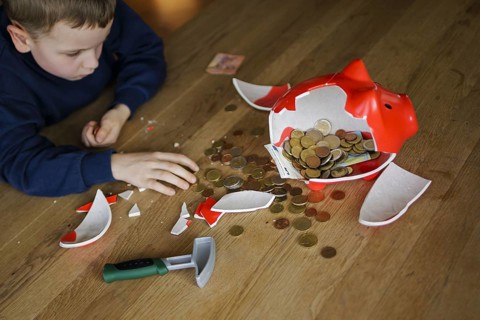 Symbolic photo on the subject of saving. A boy smashes his savings slip and counts the money it