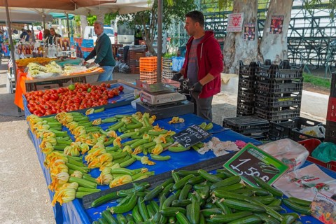 Market stall with fresh vegetables such as courgettes and peppers. A vendor stands behind the