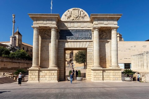 A monumental entrance with reliefs and columns under a blue sky, Cordoba