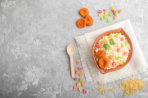 Bulgur porridge with dried apricots and candied fruits in clay bowl on a gray concrete background