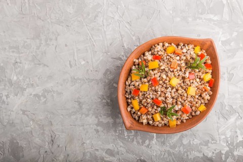 Buckwheat porridge with vegetables in clay bowl on a gray concrete background. Top view, flat lay,