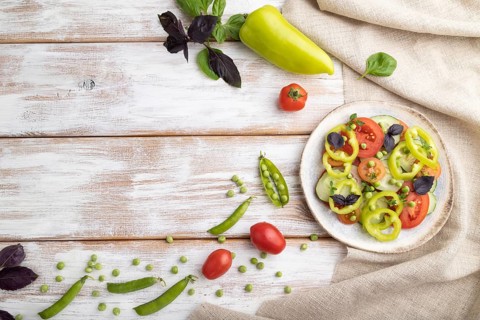 Vegetarian salad from green pea, tomatoes, pepper and basil on white wooden background and linen