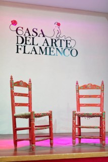 Two decorative red chairs on a stage under the lettering 'Casa Del Arte Flamenco', Granada