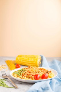 Corn noodles with tomato sauce and arugula on a gray and orange background and blue textile. Side
